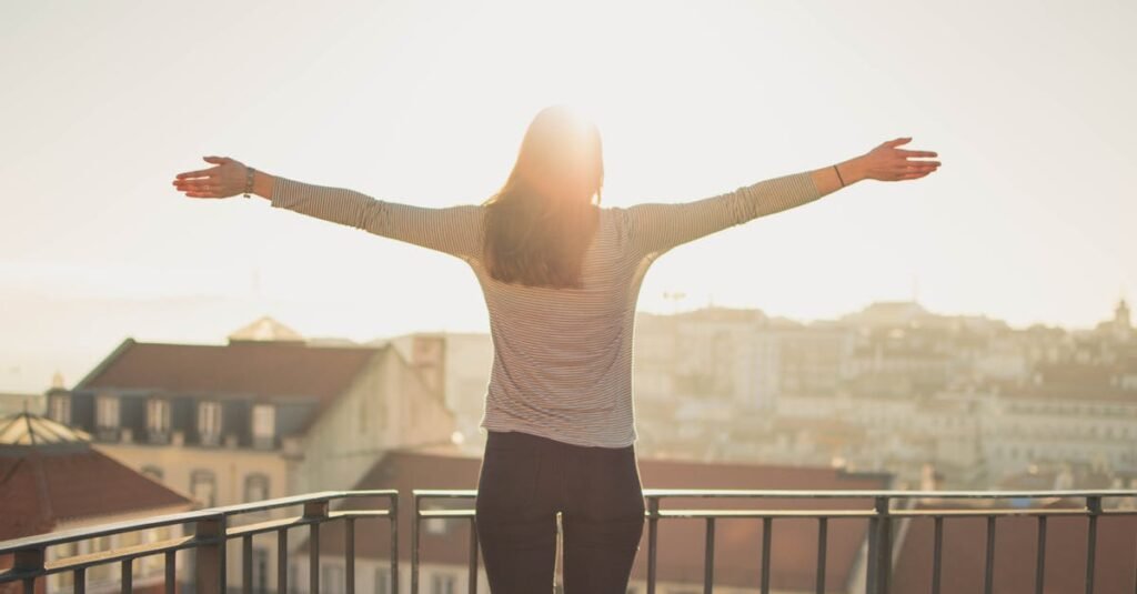 pexels photo 103127 103127 A woman stands with outstretched arms on a sunny balcony, embracing the morning light.