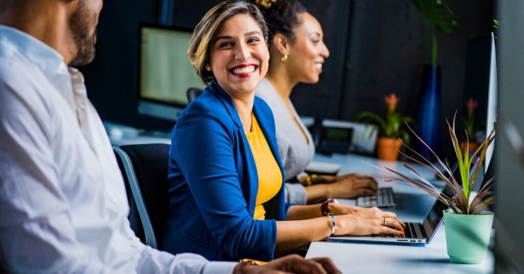pexels photo 2422293 2422293 Three diverse professionals working and smiling at office desks, fostering teamwork and collaboration.