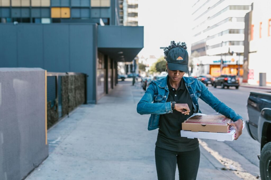 A woman delivering pizza boxes in an urban setting, showcasing city life and delivery service. (side hustle)