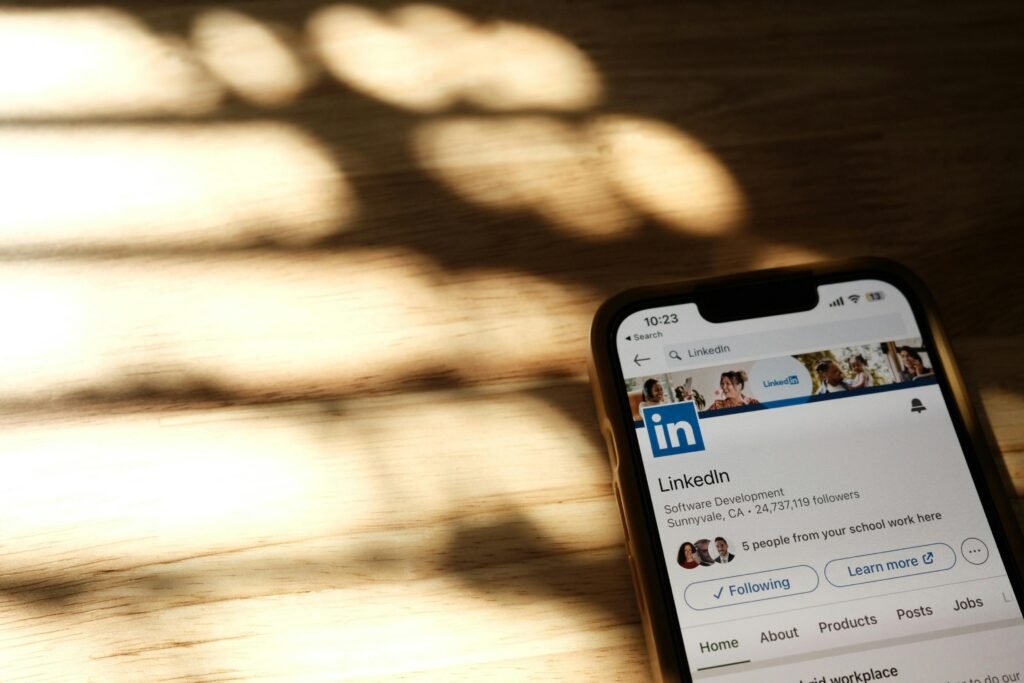 pexels-photo-16450744-16450744 Close-up of a smartphone showing a LinkedIn profile page on a wooden table with shadows.