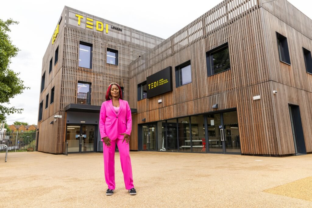 A stylish woman in a bright pink suit poses confidently outside TEDI-London campus.