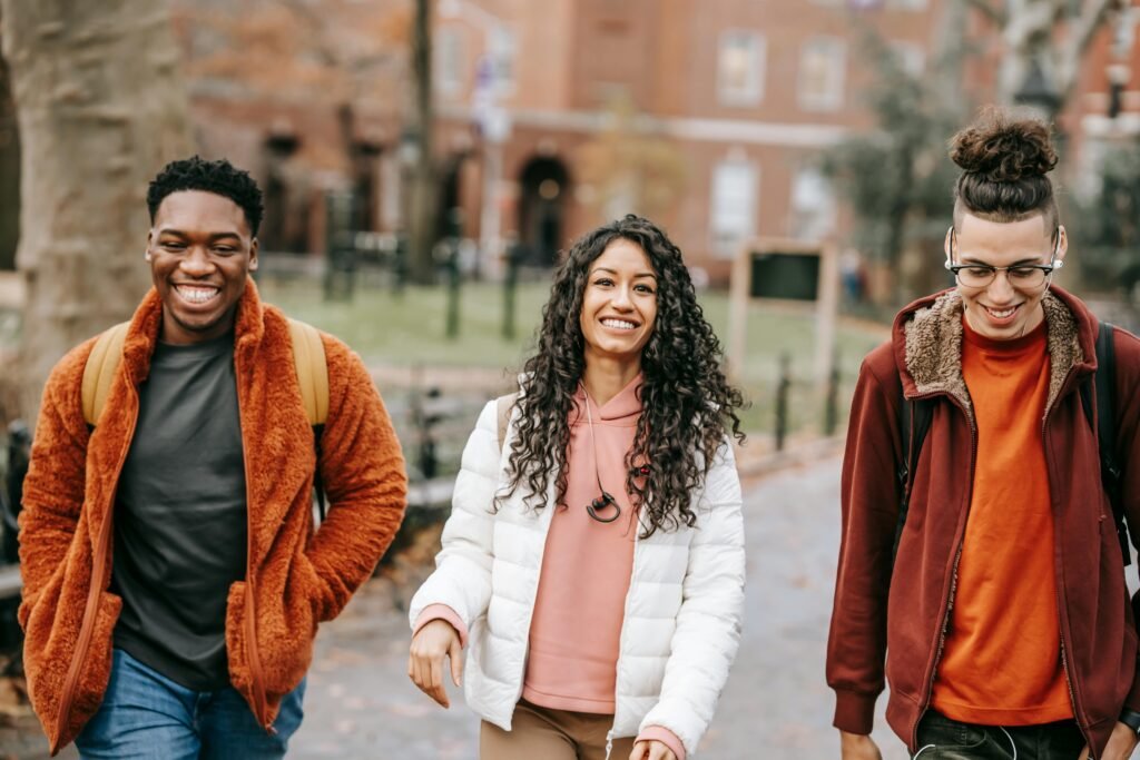 Happy multiracial friends in trendy outfits smiling while strolling together in city park