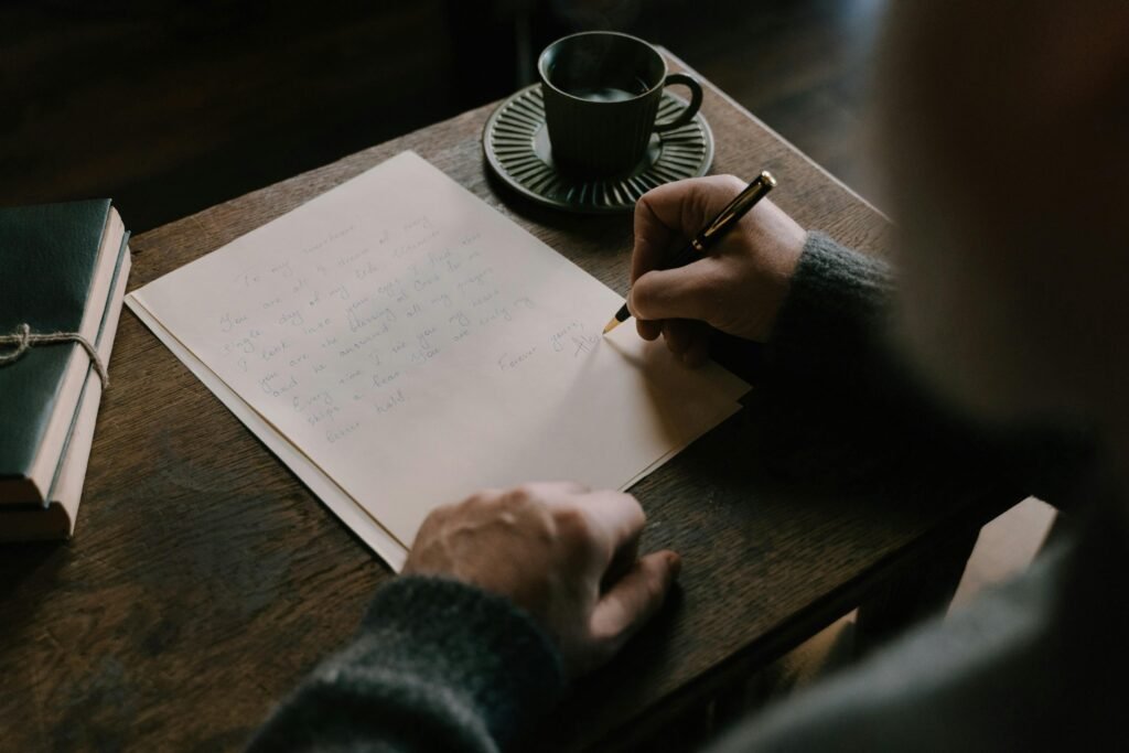 pexels-photo-6830863-6830863 An adult writing a scholarship letter on a wooden desk with a cup of coffee, embodying a warm, intimate atmosphere.